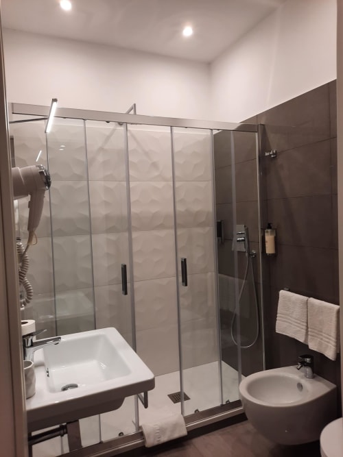 Bagno moderno nella Maritza Guest House Roma con box doccia in vetro, lavabo bianco, wc, piastrelle scure e portasciugamani bianco