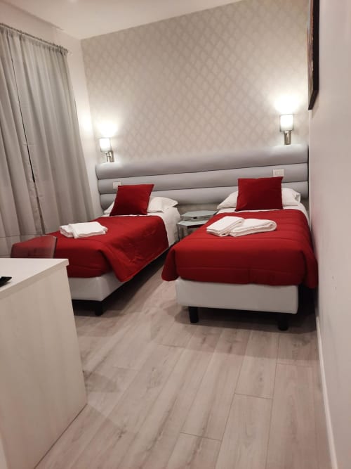 Camera doppia della Maritza Guest House a Roma con coperte rosse, cuscini bianchi, testiera rivestita grigia e arredi moderni