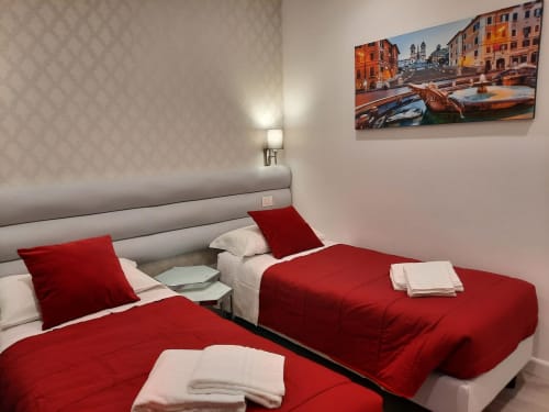 Camera matrimoniale moderna presso Maritza Guest House Roma con biancheria rossa, opere d'arte con vista città, applique da parete e design contemporaneo