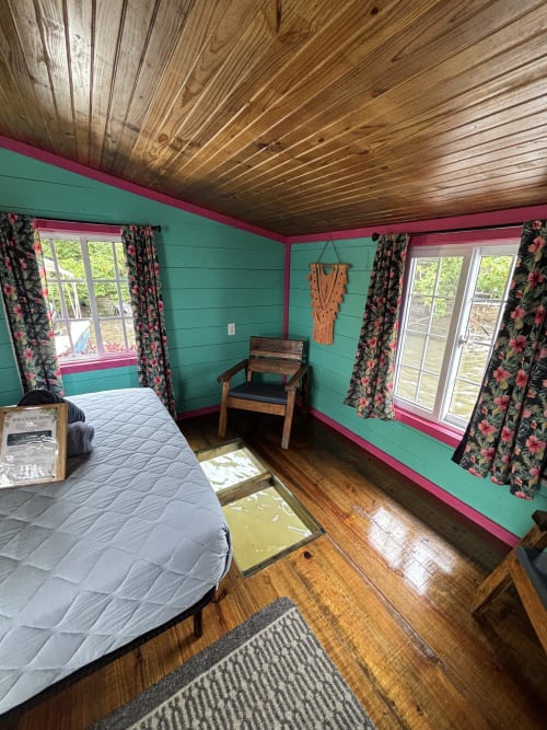 Bright turquoise and pink overwater room at BarrBra BnB in Bocas del Toro with wooden ceiling, bed, chair, and floral