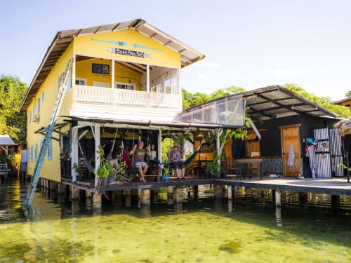 Overwater bungalow at BarrBra BnB in Bocas del Toro with yellow main house, guests on deck, turquoise water