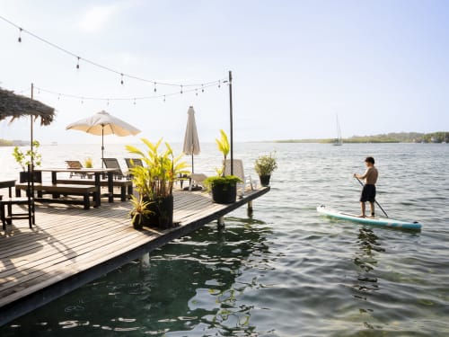 Waterfront deck at BarrBra BnB in Bocas del Toro with paddle boarder, umbrellas, and lounging area