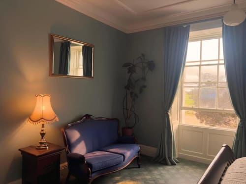 Chambre élégante à South Hill House avec canapé bleu, lampadaire, miroir et grande fenêtre sur la campagne de Delvin