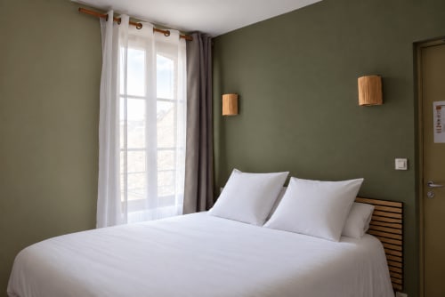 Chambre moderne de l'hôtel Au Bon Séjour avec murs vert sauge, literie blanche, touches boisées et vue sur la ville