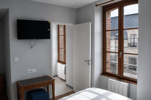 Modern hotel room at Au Bon Séjour with TV, wooden furniture, radiator, and city view through large windows