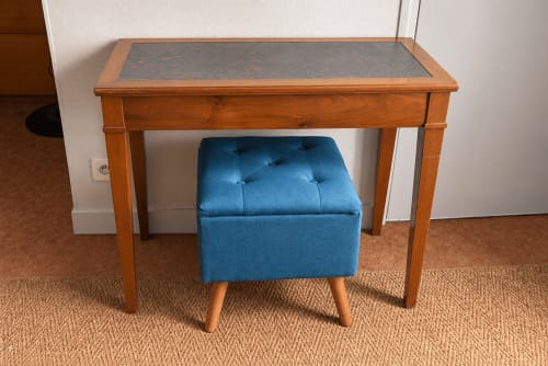 Wooden desk with slate top and blue tufted ottoman stool in hotel room at Au Bon Séjour