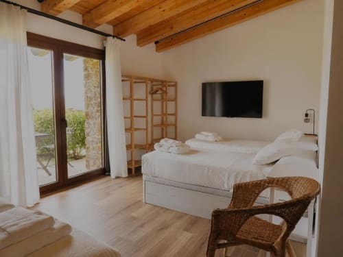 Habitación espaciosa del Hotel Izarbe en Burgos con ropa de cama blanca, vigas de madera, TV, silla de mimbre y acceso a terraza