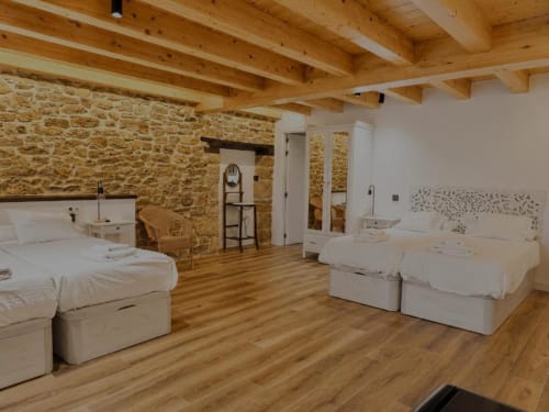 Amplio dormitorio rústico en Hotel Izarbe de Burgos con muros de piedra, vigas de madera y camas blancas
