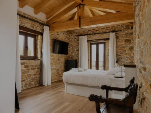 Habitación de lujo en Hotel Izarbe en Burgos con muros de piedra vista, vigas de madera y elegante ropa de cama blanca