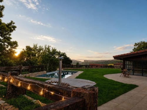 Patio exterior del Hotel Izarbe en Burgos con piscina, jardín cuidado, muebles de madera y vistas a las montañas al atardecer