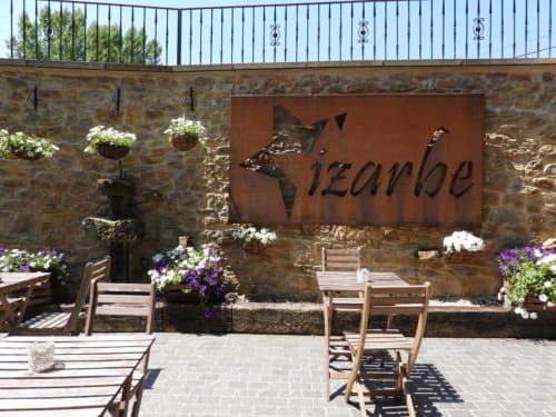 Patio del Hotel Izarbe en Burgos con asientos de madera, muros de piedra, macetas con flores y señalética decorativa de metal.
