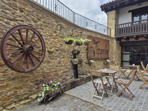 Patio del Hotel Izarbe en Burgos con muros de piedra rústica, rueda de carro de madera y zona de estar al aire libre