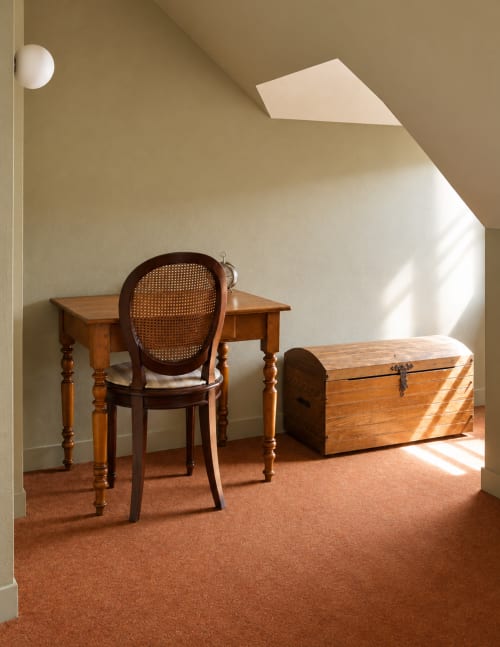 Sunlit attic workspace at Au Bon Séjour with wooden desk, caned chair, and antique trunk in Sainte-Suzanne-et-Chammes