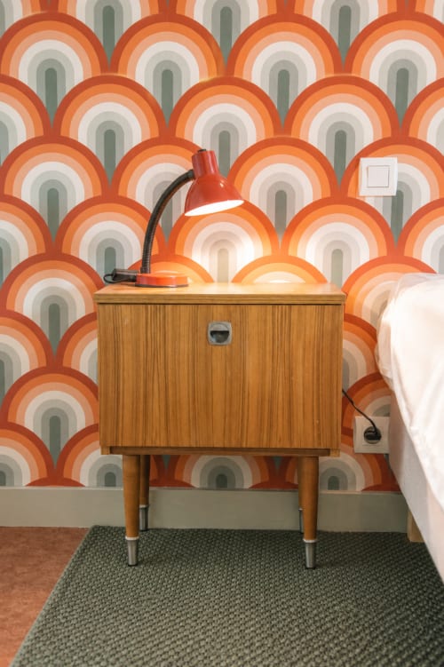 Retro-style bedroom at Au Bon Séjour with mid-century wooden nightstand, orange desk lamp, and vintage patterned wallpaper