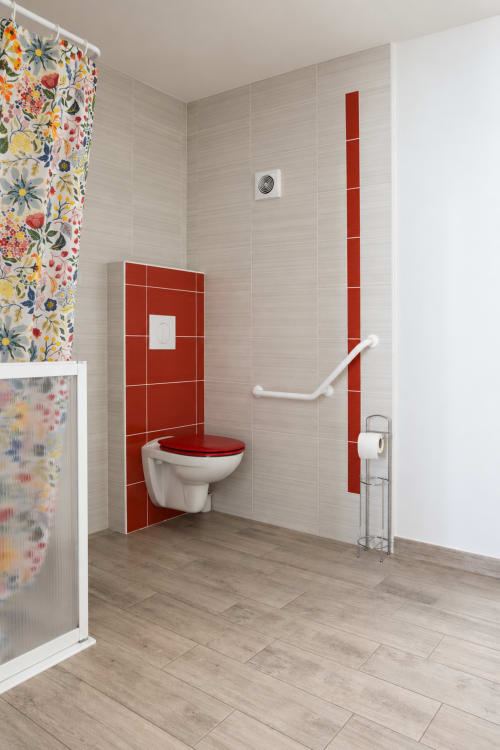 Accessible bathroom at Au Bon Séjour with red tile accents, grab bars, and roll-in shower facilities