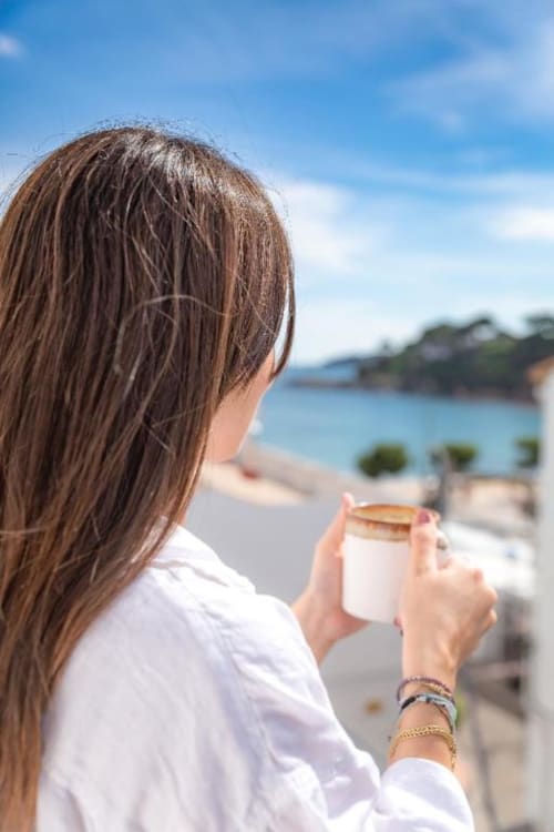 Mujer sosteniendo una taza de café en el balcón con vistas a la playa de Llafranc y el Mar Mediterráneo en el Hotel La Muntanya