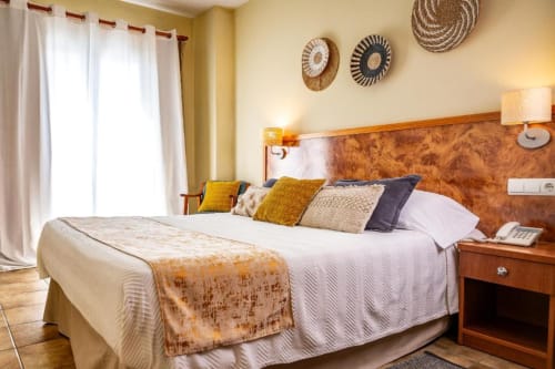 Cálida habitación costera en Hotel La Muntanya en Llafranc con cabecero de madera, almohadas en capas, balcón con vista al mar y