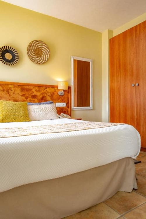 Luminosa habitación doble en Hotel La Muntanya con paredes amarillas, cabecero de madera, ropa de cama blanca y armario naranja