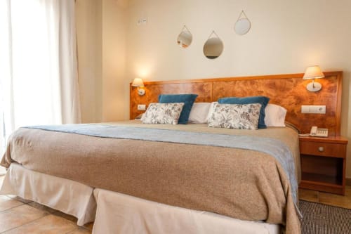 Dormitorio de lujo King Size en Hotel La Muntanya en Llafranc con cabecero de madera, almohadas azules y espejos colgantes