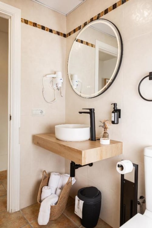 Lavabo moderno con lavamanos de cerámica blanca, grifo negro y espejo redondo en el Hotel La Muntanya de Llafranc
