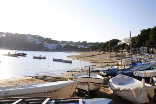Cala de Llafranc con barcas de pesca fondeadas, playa arenosa y casas blancas mediterráneas en la ladera