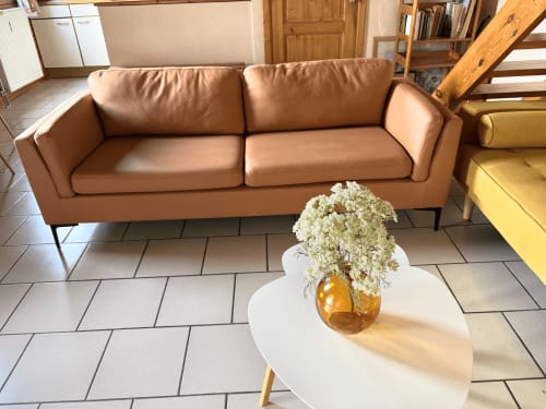 Salon cosy du gîte Aux 4 Chalets Corbion avec canapé en cuir beige, table d'appoint blanche et vase ambre avec gypsophile