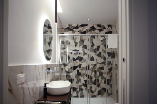 Bagno moderno a Totonno's Rooms a Tropea con doccia in piastrelle geometriche, lavabo rotondo e specchio illuminato