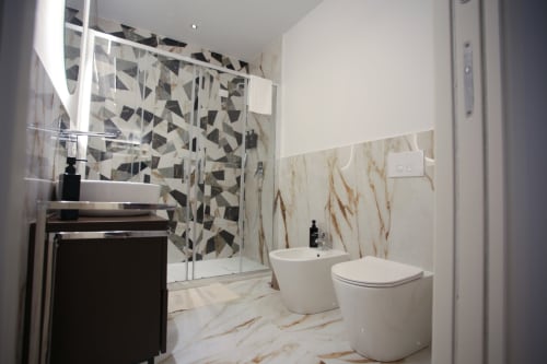 Bagno moderno alle Camere Totonno di Tropea con pavimenti in marmo, pareti doccia a motivi geometrici, sanitari bianchi e