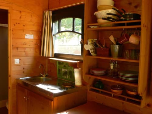 Cuisine rustique en bois avec évier, cuisinière et étagères ouvertes présentant vaisselle et ustensiles au Relais de Maufront