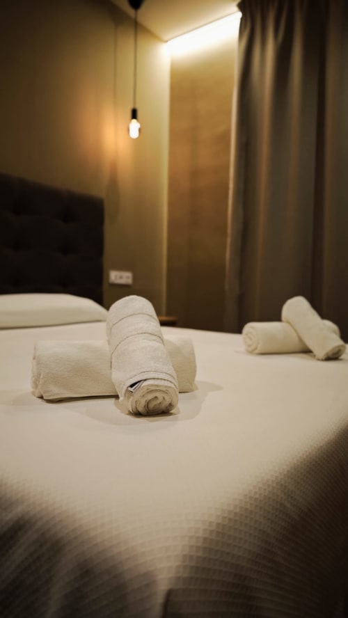 Toallas blancas enrolladas en cama premium del Hotel Continental Calella, habitación cálida con cabecera oscura