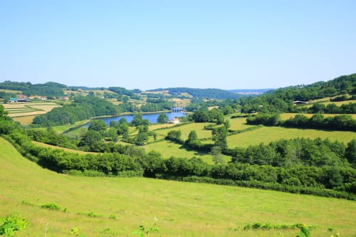 Paysage champêtre pittoresque près du Relais de Maufront à Ouagne avec champs verdoyants, lac bleu et ferme lointaine
