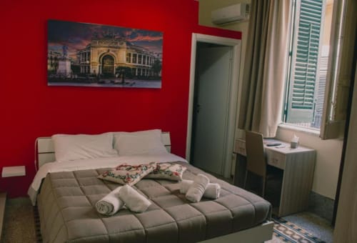 Camera doppia luminosa a Mizzica Rooms a Palermo con parete rossa, letto confortevole, comfort moderni e vista sulla città