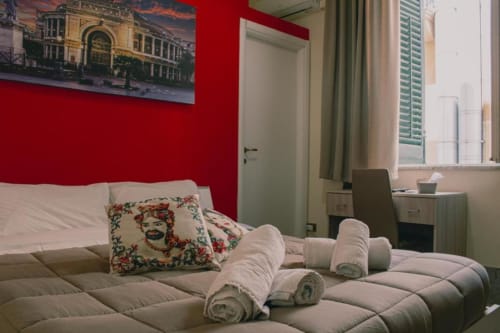 Accogliente camera doppia di Mizzica Rooms Palermo con parete rossa, asciugamani arrotolati, cuscino decorativo e scrivania vicino finestra