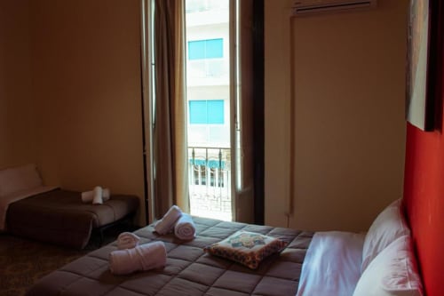 Camera tripla dell'hotel Palermo con balcone vista città, letti matrimoniali, asciugamani arrotolati e arredamento moderno