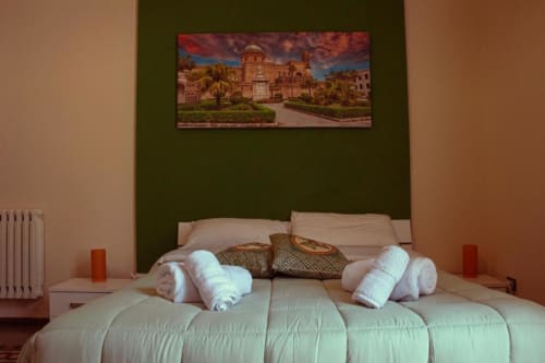 Camera tripla presso Mizzica Rooms Palermo con biancheria bianca, asciugamani arrotolati e vista sulla città raffigurata sulla testata oliva.