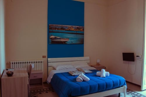 Luminosa camera quadrupla alle Mizzica Rooms di Palermo con letti blu, testata bianca, opere d'arte con vista città e servizi moderni