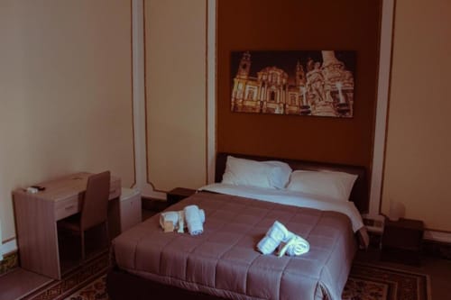 Camera quadrupla presso Mizzica Rooms a Palermo con biancheria bianca e marrone, scrivania e quadri con architetture locali