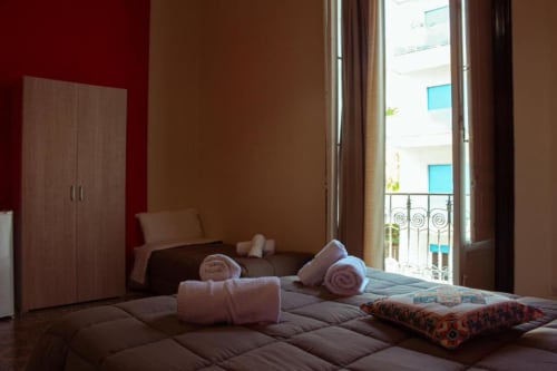 Camera tripla luminosa a Mizzica Rooms di Palermo con balcone vista città, asciugamani arrotolati e arredamento moderno