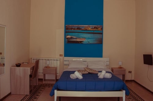Camera quadrupla a Mizzica Rooms a Palermo con letto matrimoniale blu, cuscini bianchi, arte nautica e vista sulla città