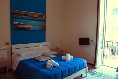 Luminosa camera quadrupla presso Mizzica Rooms a Palermo con biancheria blu, arte costiera, balcone, TV e vista città