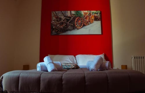 Camera moderna a Mizzica Rooms a Palermo con divano marrone, cuscini bianchi e quadro colorato su parete rossa