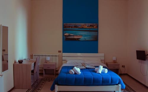 Camera quadrupla a Mizzica Rooms, Palermo con biancheria blu, opere d'arte con vedute cittadine e arredamento moderno