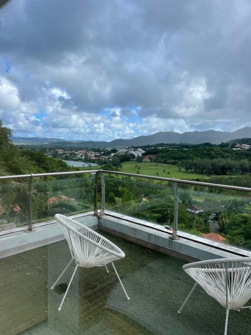 Balcon moderne aux chaises blanches surplombant une vallée verdoyante, montagnes et parcours de golf à la Résidence Thalie, Martinique