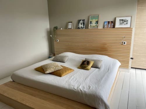 Chambre moderne avec draps blancs et coussins dorés, tête de lit en lattes de bois avec étagère, parquet clair à la Résidence Thalie