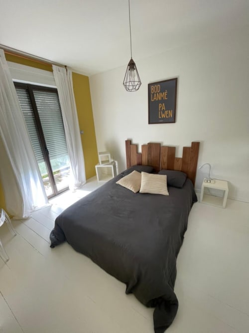Chambre moderne de la villa Les Trois-Îlets avec lit sombre, tête de lit en bois, suspension géométrique et terrasse vue mer