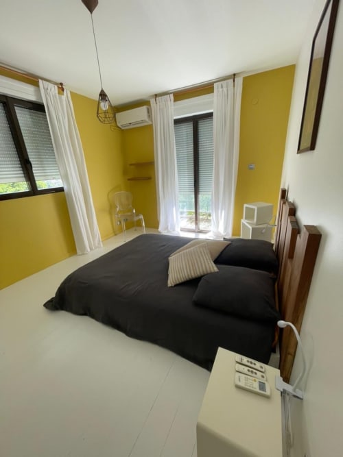 Chambre lumineuse jaune vif avec literie noire à la villa Les Trois-Îlets, rideaux blancs et portes donnant sur la mer