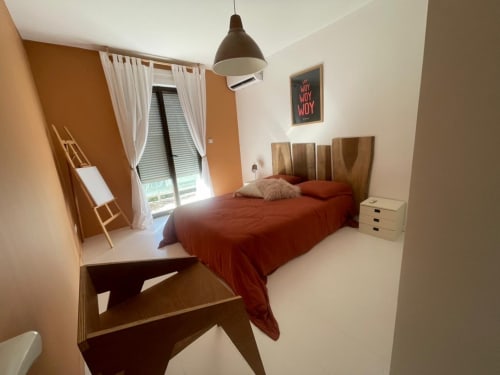 Chambre moderne de la villa Les Trois-Îlets avec literie rouge, tête de lit en bois, suspension et vue sur mer par la fenêtre