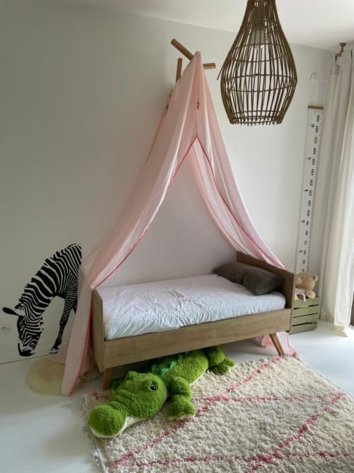 Chambre d'enfant avec lit à baldaquin rose, structure bois, jouet peluche grenouille verte, tapis rayé, lampe suspendue en rotin à Villa Thalie