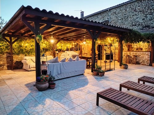 Twilight view of a pet-friendly gîte in South France with lit pergola, seating, lounge chairs, and stone villa backdrop