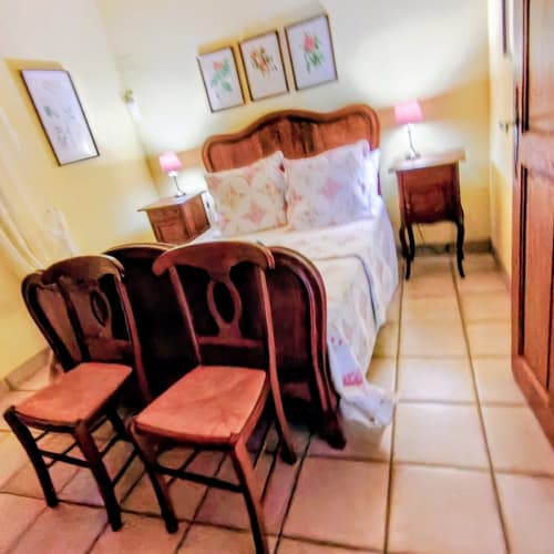 Cozy bedroom in French cottage gîte with wooden bed, red chairs, floral bedding, terracotta tile floor and yellow walls